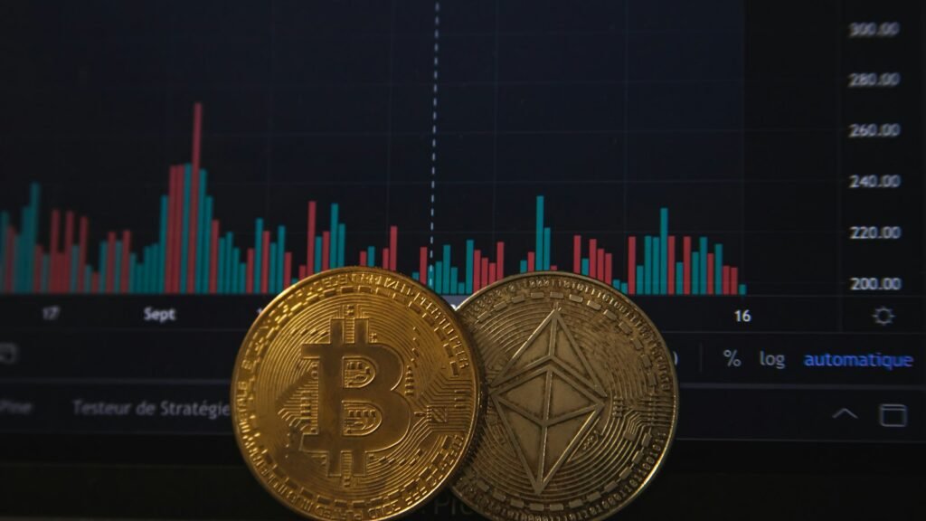 Pièces de bitcoin et d'ether posées sur un clavier devant un graphique boursier
