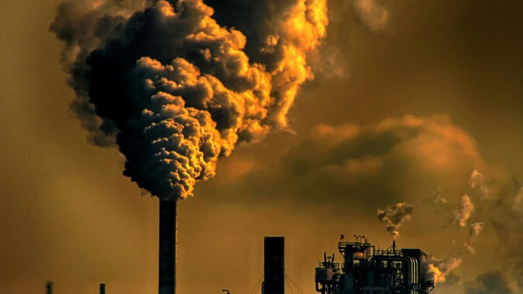 Haute cheminée industrielle rejetant une épaisse fumée sombre dans un ciel orangé