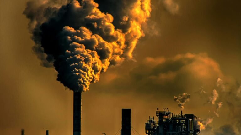 Haute cheminée industrielle rejetant une épaisse fumée sombre dans un ciel orangé