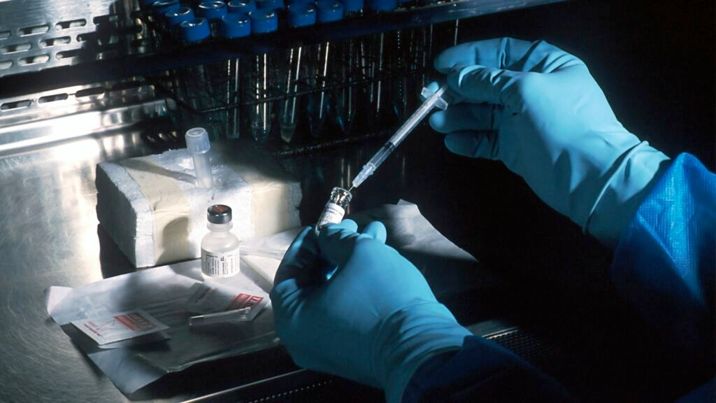 Mains gantées prélevant un vaccin dans un flacon avec une seringue